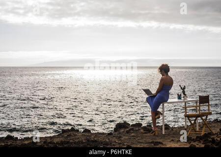 alternative office location outdoor on the ocean coast. beautiful woman work outside in a modern concept using internet and a laptop. digital nomad li Stock Photo