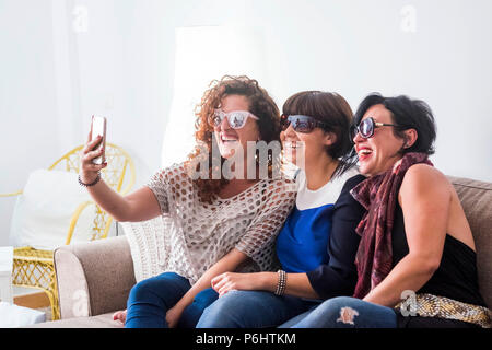 three caucasian young women friends taking selfie at home with modern smartphone. share life and crazy moment on social media. smile and enjoy using n Stock Photo