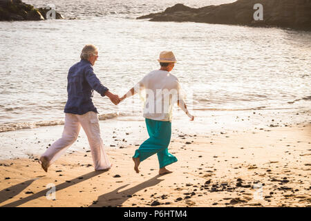 beautiful mature couple outdoor in leisure activity run together at the beach on the shore hanging the hands and living together forever. love concept Stock Photo