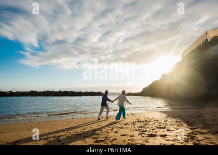 beautiful mature couple outdoor in leisure activity run together at the beach on the shore hanging the hands and living together forever. love concept Stock Photo