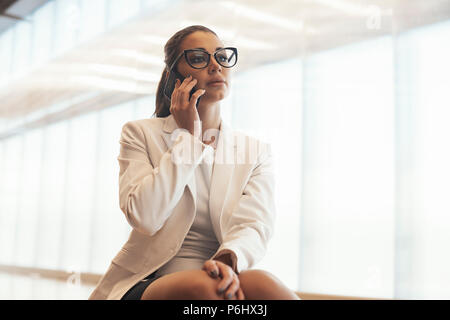 Young business spectacled woman in white jacket talking by mobile phone. Stock Photo