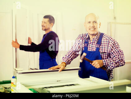 Two smiling professional workers in blue coverall with different PVC windows and doors Stock Photo