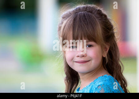 Portrait of little fashionable blond girl in blue dress, with gray eyes and beautiful long hair smiling in camera on bright blurred colorful backgroun Stock Photo