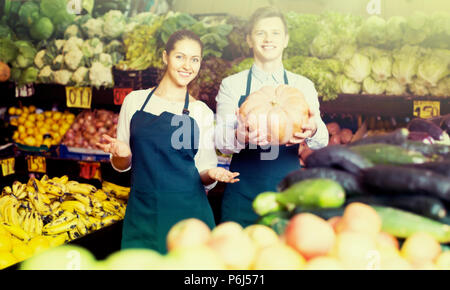 Friendly smiling market stuff offering for retail large squash . Focus on woman Stock Photo