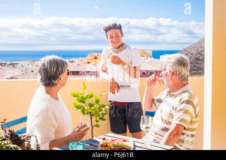 grandfathers adult mature and teenager nephew enjoy outdoor in the terrace some leisure with food and drinks. ocean and city view, vacation sunny day  Stock Photo