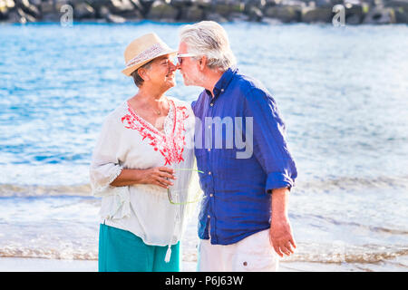 happy beautiful caucasian coule of adult senior touch noses and having fun together. smile and joke in a sunny day of vacation under the sun and ocean Stock Photo