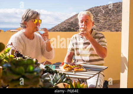 senior adult couple outdoor on the rooftop drinking somw white wine and eating some snacks food salds and fruits. sunny day of vacation or retired lif Stock Photo