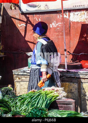 Lijiang, China - April 2015: Older married woman from the Chinese Naxi minority wearing traditional clothing while buying food at the local market Stock Photo