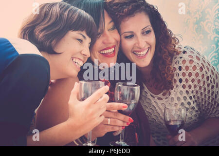 three happy and beautiful females friends have fun together at home drinking some red wine and enjoying the leisure and tie friendship. relationship w Stock Photo