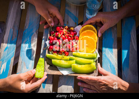 closeup of young and old hands from grandmother and teenager nephew eating some fresh season fruits on the wood table. healhty lifestyle in family out Stock Photo
