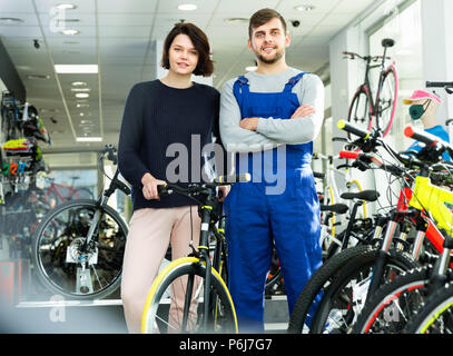 Cheerful positive young woman and seller standing with bicycle in the store indoors Stock Photo