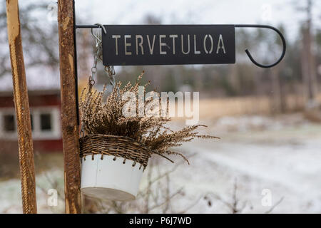 Forged metal plaque with the inscription - "Welcome" in the Finnish language, and hanging on the fence potted plants Stock Photo