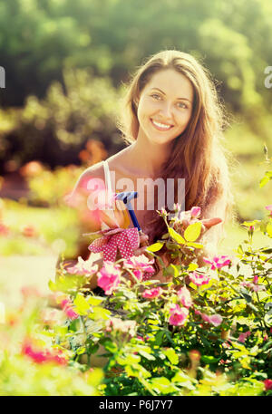 Positive smiling young female gardening with roses in yard Stock Photo
