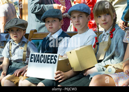 Kidderminster, UK. 30th June, 2018. A journey back in time begins on the Severn Valley Railway as we turn the clock back to the 1940s. Visitors and staff pull out all the stops to ensure a realistic WW2 wartime Britain is experienced on this heritage railway line. 1940s children, WWII war evacuees, can be seen sitting here together at Kidderminster vintage station awaiting the next steam train. Credit: Lee Hudson/Alamy Live News Stock Photo