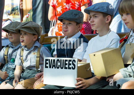Kidderminster, UK. 30th June, 2018. A journey back in time begins on the Severn Valley Railway as we turn the clock back to the 1940s. Visitors and staff pull out all the stops to ensure a realistic WW2 wartime Britain is experienced on this heritage railway line. 1940s children, WWII war evacuees, can be seen sitting here together at Kidderminster vintage station awiting the next steam train.Credit: Lee Hudson/Alamy Live News Stock Photo