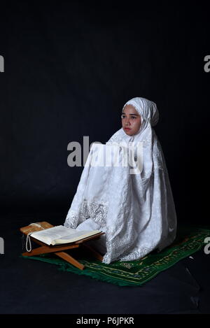 Little Muslim Girl praying after reading Koran (Quran) Stock Photo