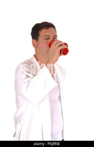 A handsome tall man standing in a white bathrobe and drinking from  a red coffee mug, isolated for white background Stock Photo