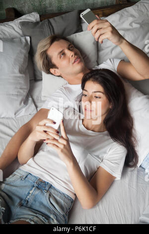 Addicted millennial couple relaxing in bed using smartphones Stock Photo