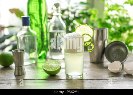 Egg Gin Fizz Cocktail with Lime Garnish. Making Gin Fizz Drink with ingredients and bar equipment. Stock Photo