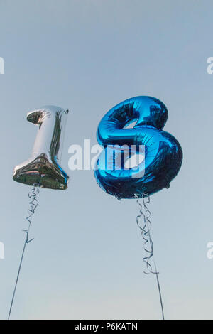 Two helium balloons celebrating an 18th Birthday party against a blue sky at dusk Stock Photo