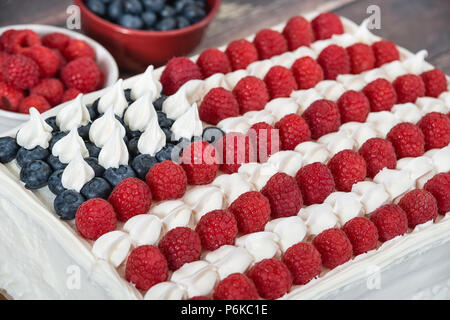 Patriotic, red white and blue, American flag cake. Fresh blueberries and raspberries in the background. Concept for Fourth of July celebration. Stock Photo