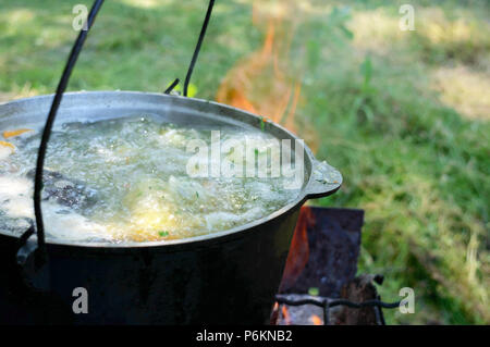 Fish soup boils in cauldron at the stake on the nature. Soup in a pot in the fire.  Close-up. Stock Photo