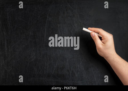 Male hand holding white chalk on blank blackboard. Stock Photo