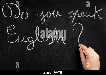 Do you speak English question handwritten on used chalkboard by male hand holding white chalk Stock Photo