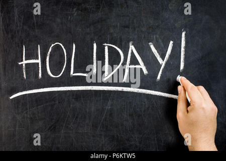 Hand with white chalk underlining handwritten holiday text on dirty blackboard Stock Photo