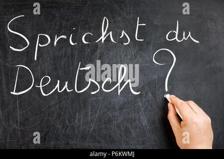 Do you speak German question handwritten on dirty chalkboard by male hand holding white chalk Stock Photo