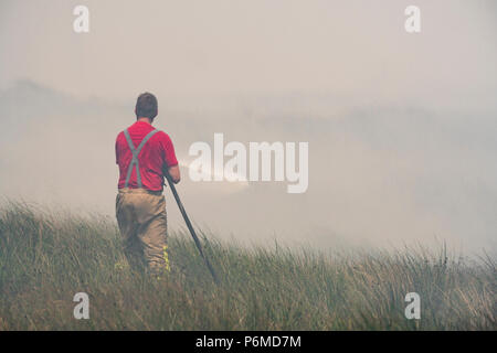 Lancashire, UK. 1 July 2018 - A male firefighter attempts to control the growing moorland fire on Winter Hill and Rivington Pike which was started a number of days ago. Fire crews from across the UK have converged on Winter Hill to control the blaze which is growing by metres per hour. Lancashire Fire and Rescue and Lancashire Police are leading the response to the 'major incident'. Credit: Benjamin Wareing/17�Թ����� Live News Stock Photo