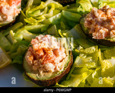 Sliced filled avocados with prawns and crabmeat on a bed of baby gem lettuce with lemon wedges on outdoor table in sun Stock Photo