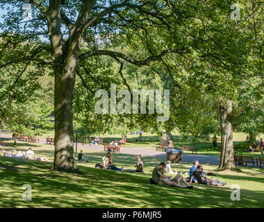 Couple hugging sitting on grass and people relaxing in Princes Street Gardens in the shade under trees during heatwave, Edinburgh, Scotland, UK Stock Photo