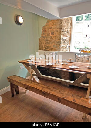 Wooden trestle table set with china cups, saucers, plates and cutlery ready for serving afternoon tea in Kavanagh's Tea Rooms Oakham, Rutland, UK Stock Photo