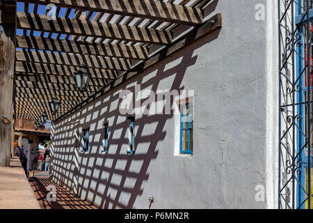 Shadows and sidewalks. The wooden trellis casts a beautiful shadow against the adobe wall along a sidewalk located in Old Town Albuquerque New Mexico Stock Photo