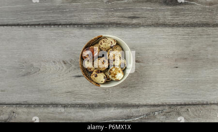 Table top view - small ceramic bowl full of spotted quail eggs on gray wood desk. Stock Photo