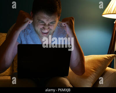Happy man watching something on a laptop. Winning. Evening activities at home. Stock Photo