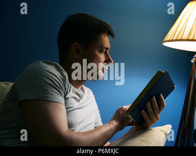 Man on a sofa is reading the book at the evening. Stock Photo