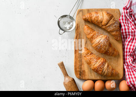 Croissants and ingredients for baking on concrete background with copy space for text. Eggs, flour, rolling pin, kitchen textile and pastry Stock Photo