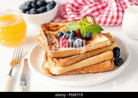 French toast with fresh blueberries, raspberries and honey on white plate. Tasty breakfast Stock Photo