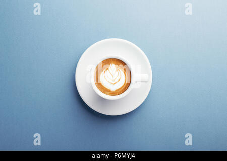A cup of cappuccino with beautiful latte art on blue background. Top view, central composition. Stock Photo