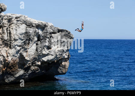 11-year-old boy jumping from a cliff into the sea in Salento, Italy. Stock Photo