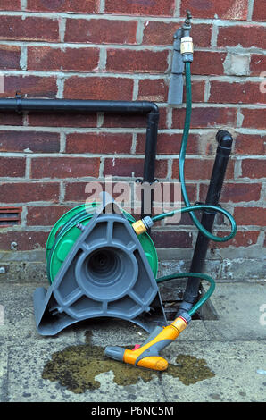 Hosepipe reel connected to a standpipe in garden, with leaking water Stock Photo