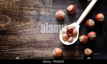 Nuts on a wooden table. Hazelnuts in the shells and shelled. A wooden spoon and nuts on brown table. Stock Photo