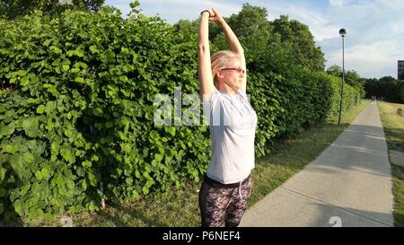 Healthy lifestyle woman in sportswear stretching leg muscles preparing for a run in the park in summer. Healthy athlete full body, touching feet doing legs stretches getting ready for outdoor workout. Stock Photo