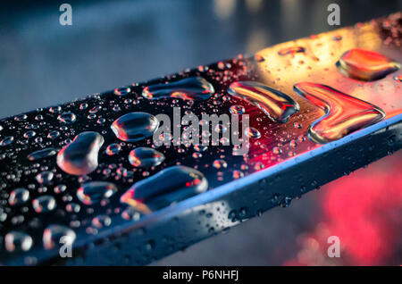 Raindrops on the metal or stainless steel handrail surface in the light colored lights. Closeup photography with film grain. Stock Photo