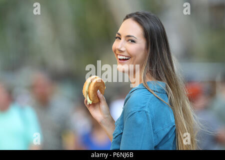 Happy woman holding a burger looking at you on the street Stock Photo