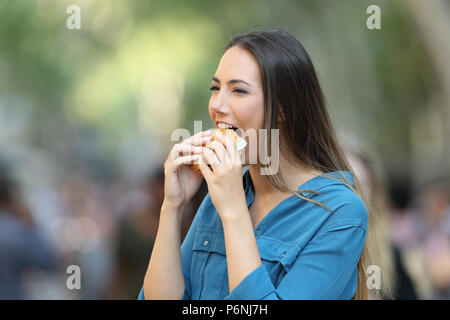 Portrait of a happy woman eating a burger walking on the street Stock Photo