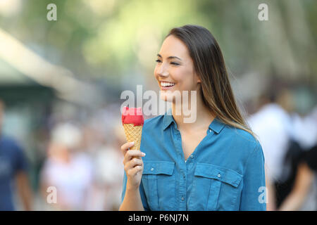 Happy woman holding an ice cream and looking away walking on the street Stock Photo