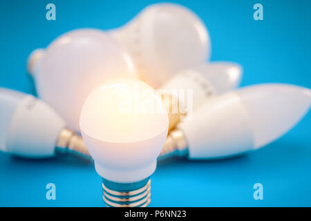 Idea concept with light bulbs. Shining LED lamp and bunch of other light bulbs on blue background Stock Photo